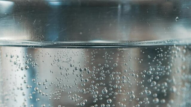 Glass water in side view with surface tension and fresh sparkling water in a glass tumbler with bubbles and swirls. Clear glass beaker with water