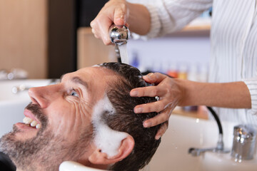 Obraz na płótnie Canvas female barber washing head of male client in barbershop