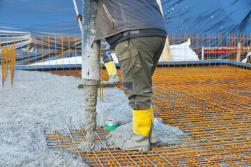 Bauarbeiter gießen die Bodenplatte eines Einfamilienhaus-Neubaus über der Baustahlmatte mit der...