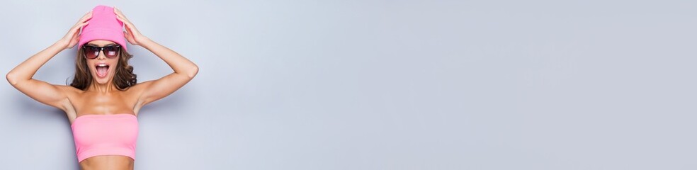 Excited young woman in pink clothes touching her head against grey background