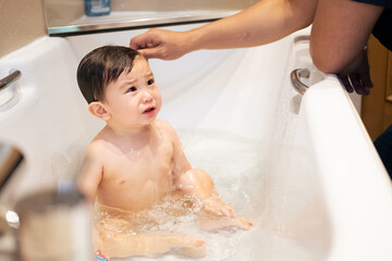 An unrecognizable new dad washing and giving his multiracial Asian male infant a bath in the...