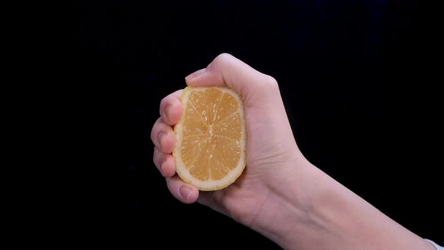 Woman squeezing a lemon half on black background. Citrus fruit source of vitamins and health concept. Slow motion