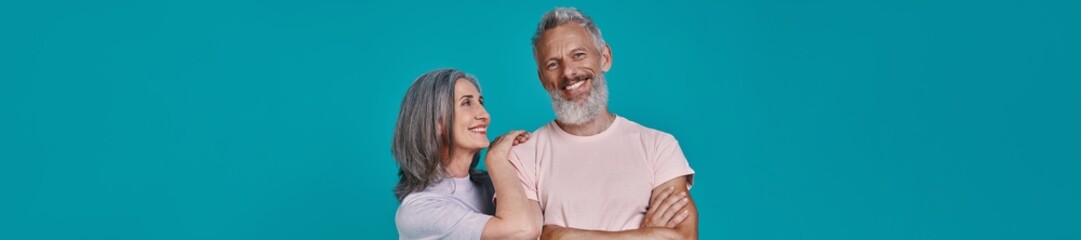 Beautiful senior couple smiling while standing together against blue background