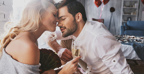 Young loving couple holding champagne flutes while sitting face to face indoor