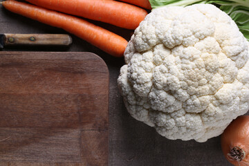 Cauliflower, brown chopping board and cooking ingredients on wooden background with copy space 