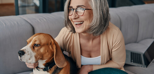 Happy senior woman spending time with her dog while sitting on the sofa at home
