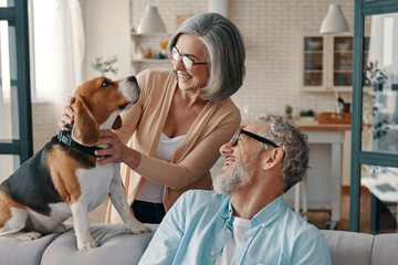 Happy senior couple smiling and taking care of their dog while spending time at home together