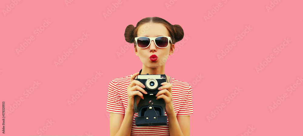 Wall mural Portrait of happy young woman photographer with film camera, female with cool girly hairstyle on pink background