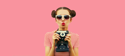 Portrait of happy young woman photographer with film camera, female with cool girly hairstyle on pink background
