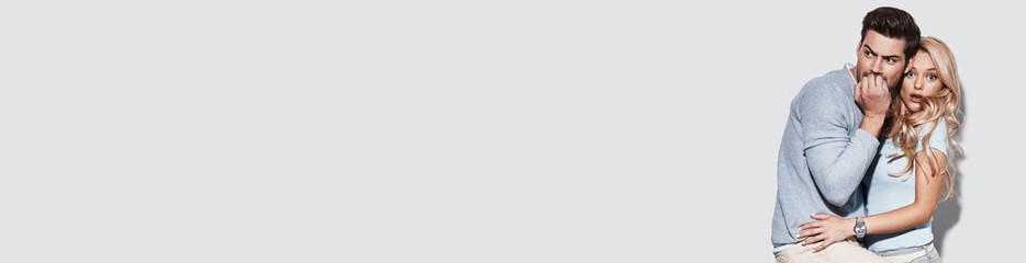 Young couple looking terrified while standing against grey background together