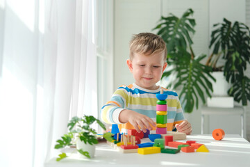 A little boy plays with wooden toys and builds a tower. Educational logic toys for children. Montessori games for child development. Children's wooden toy.