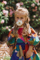 Summer spring portrait of pretty little girl wearing  dress, posing in rose garden smelling flowers. Happy smiling baby. Love of nature. spring mood