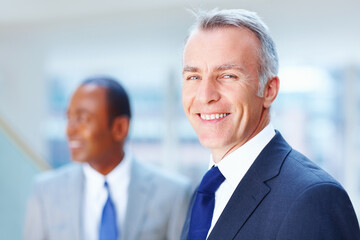Senior executive smiling with colleague in background. Focus on older Business man with colleague in background.