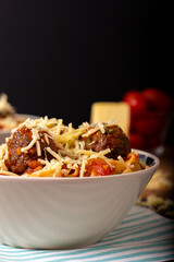 Classic italian tagliatelle spaghetti pasta with tomato sauce, meatballs, parmesan cheese and basil in plate on dark table. Dark food, dark mood