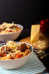 Classic italian tagliatelle spaghetti pasta with tomato sauce, meatballs, parmesan cheese and basil in plate on dark table. Dark food, dark mood