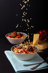 Classic italian tagliatelle spaghetti pasta with tomato sauce, meatballs, parmesan cheese and basil in plate on dark table. Dark food, dark mood
