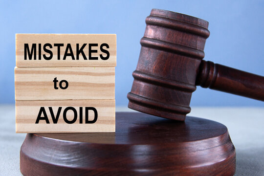 The words MISTAKES to AVOID on wooden cubes against the background of the judge's gavel and stand.