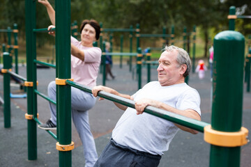 Aged man doing exercises on sports bars in open-air sports area