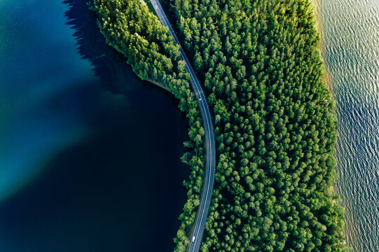 Aerial view of road in green woods and blue lakes water in Finland