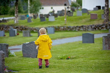 Sad little child, blond boy, standing in rain on cemetery, sad person, mourning