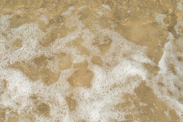 Transparent wave with white foam over the golden sand. Crystal clear sandy beach. Background with eco friendly place for rest.