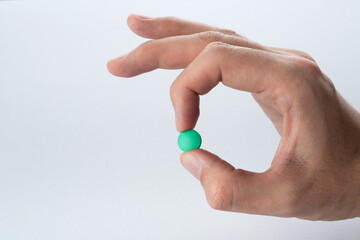Male hand holding a green pill on a grey background. Close up