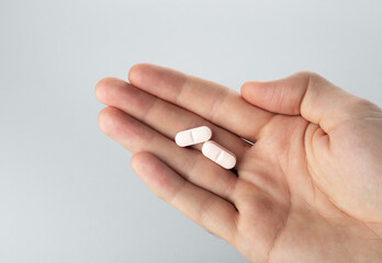 Male hand holding two pills in hand on grey background, taking Your medication. Close up