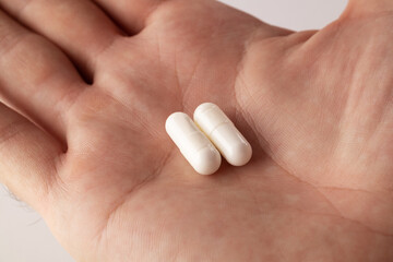 Naklejka premium Male hand holding two pills in hand on grey background, taking Your medication. Close up