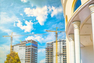 Construction cranes and unfinished modern skyscrapers against the backdrop of a classic building. New architectural solutions to replace the old ones.