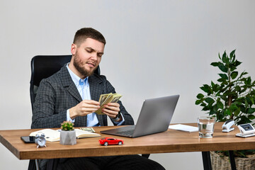 young bearded businessman working on laptop and holding money