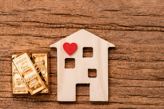 House model with heart and the gold bar with growing value put on the old wood in the office, Saving for buy house or loan for business investment real estate concept.