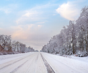 Winter dull landscape with ice-covered road and trees at side of the road.