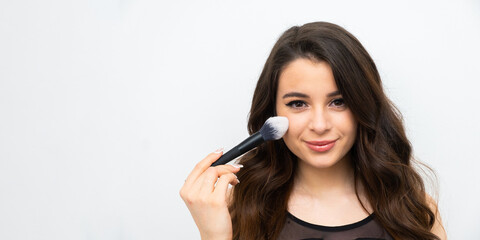 Attractive brunette holding a cosmetic brush near her face on the banner with copy space. Advertising of a beauty salon concept. 