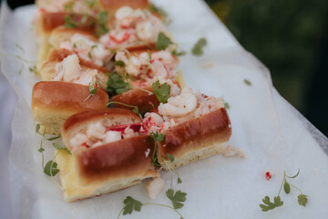 mini lobster rolls with herb garnish on white platter being served at summertime event
