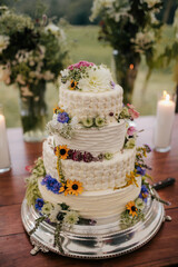 beautiful four tier wedding cake decorated with wild flowers sitting on dessert table at country wedding