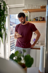 Young pensive man using mobile phone, reading news, working online in home office