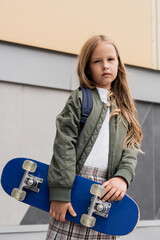 stylish preteen girl in bomber jacket holding penny board near mall.