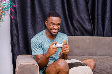 African American young joyful man resting at home sitting on couch and playing video games