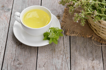 Fresh natural green melissa herbal tea in white cup. Organic aromatherapy relaxation medical healthy beverage. Rustic wooden table background. Rustic style natural light.