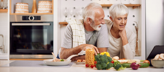 a happy senior couple preparing a healthy meal together, using a tablet