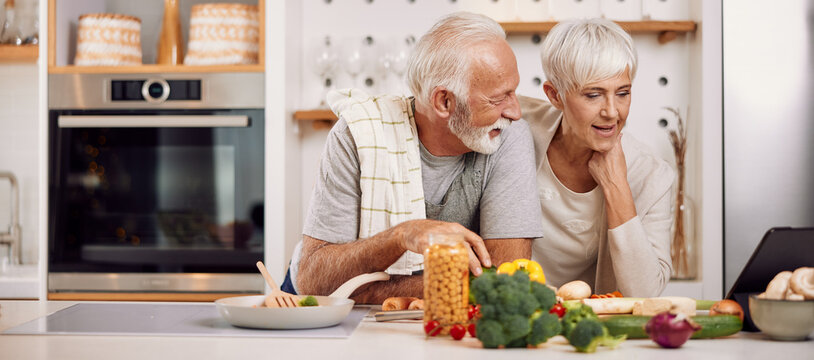 a happy senior couple preparing a healthy meal together, using a tablet