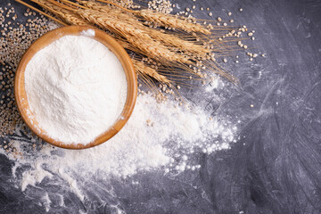 Wheat flour in a wooden bowl With wheat ears on the table, black background. - top view