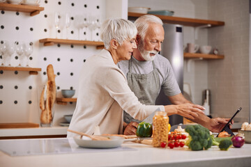 a happy senior couple preparing a healthy meal together, using a tablet
