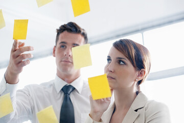 Bringing their ideas to the forefront. a coworkers arranging sticky notes on a glass wall during a...