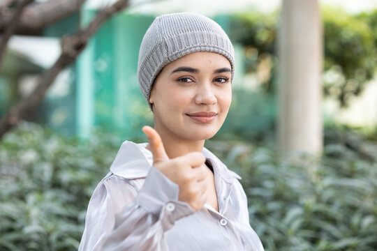 Happy smiling south asian Indian woman cancer patient wearing head scarf for hair loss after chemotherapy and radiation therapy but showing confident thumb up for good positive and satisfactory result