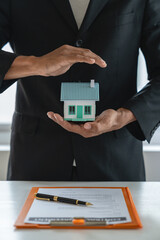 Hand covered, miniature home defense with contract paper on insurance concept. Home coverage for taking care of people in their homes. real estate project The concept of life and property insurance. - obrazy, fototapety, plakaty
