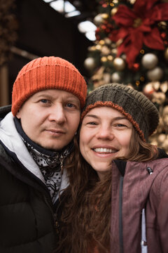 Vertical selfie of couple in love wearing hats and winter clothes at christmas tree background