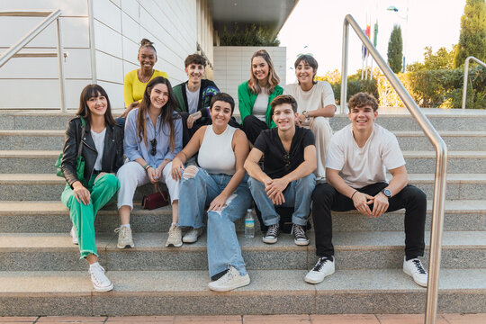 Group of nine young student friends sitting on steps at the university after class smiling and looking at the camera