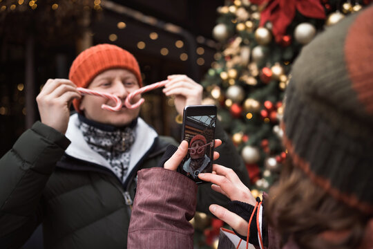 child free couple wearing hats and winter clothes taking pictures by phone at christmas city market