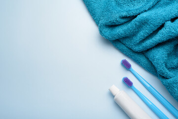 Toothbrushes with paste tube and towel on blue background.